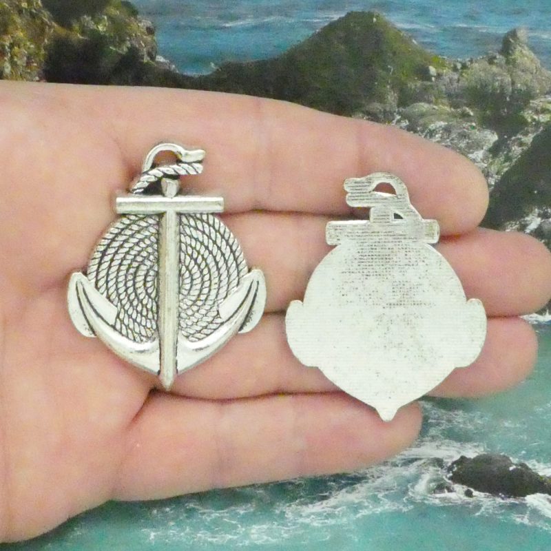 Front and back view of silver anchor charm on bare hand with coastal photo background